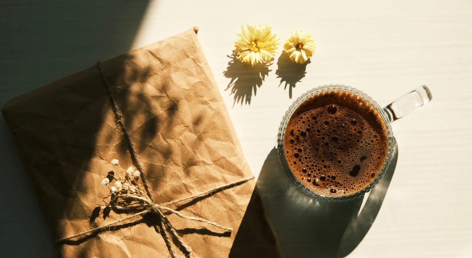Presente embrulhado em papel kraft com flores secas, numa mesa ao sol
